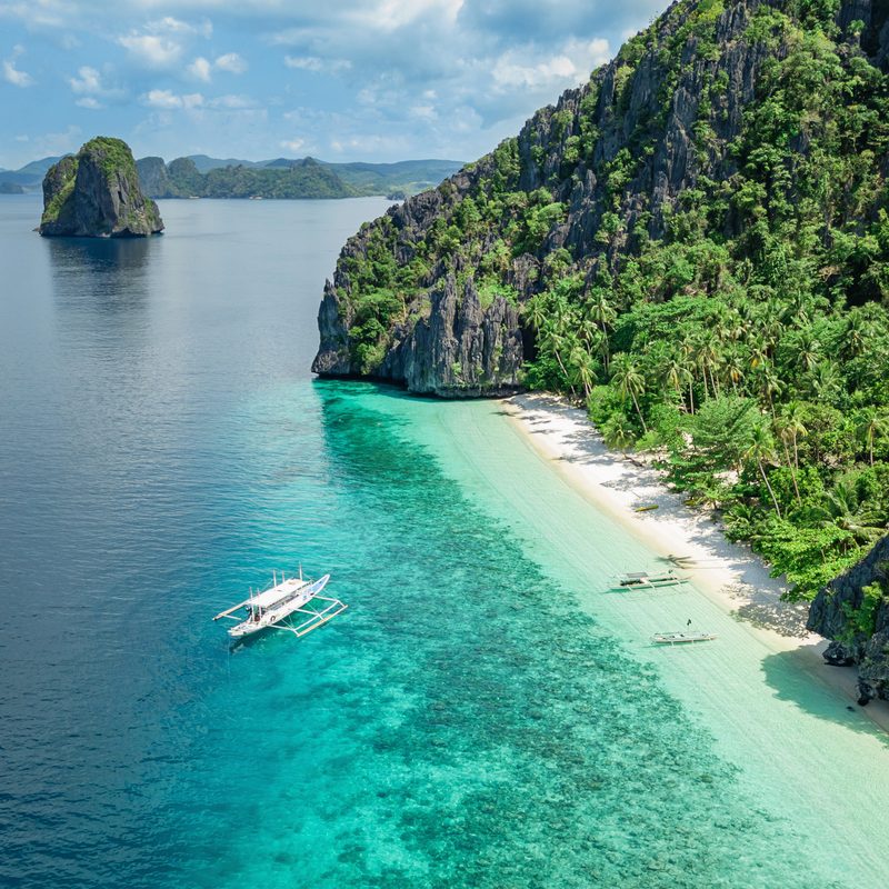 Turquoise water and limestone cliffs along a beach in El Nido.